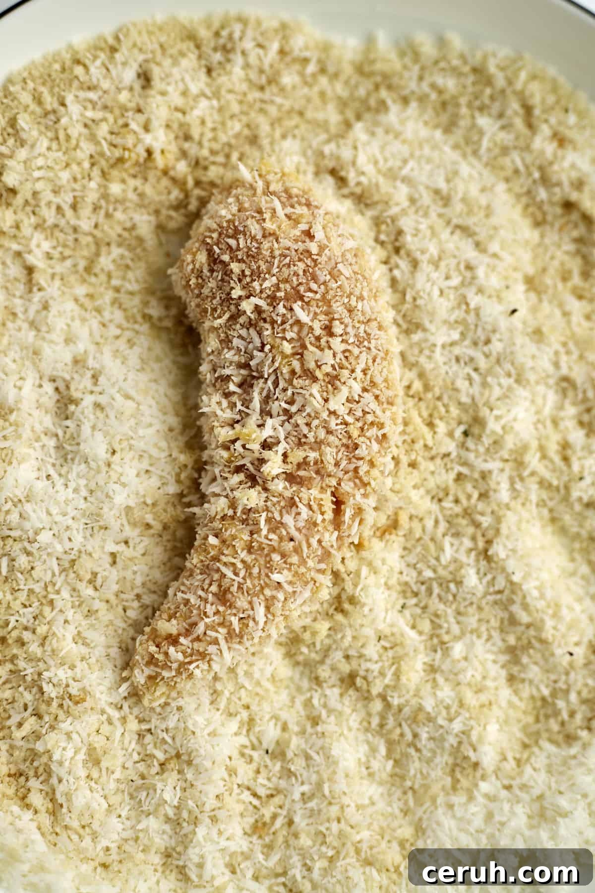 a raw chicken tender in a breadcrumb mixture