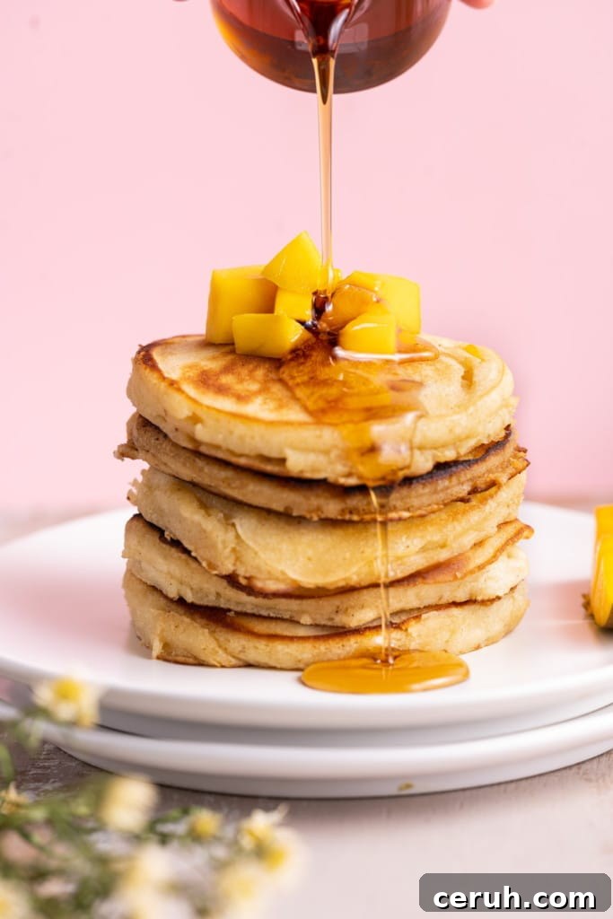 Pouring maple syrup over a stack of 5 mango pancakes