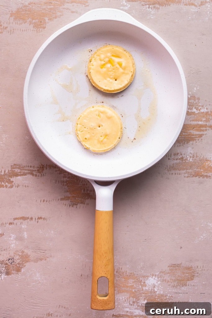 Frying two perfectly round mango pancakes in a frying pan with butter