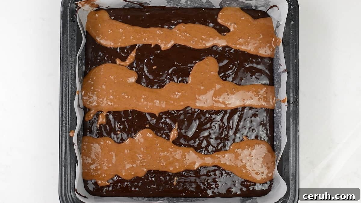 drizzling Biscoff spread over brownie batter in a square tin