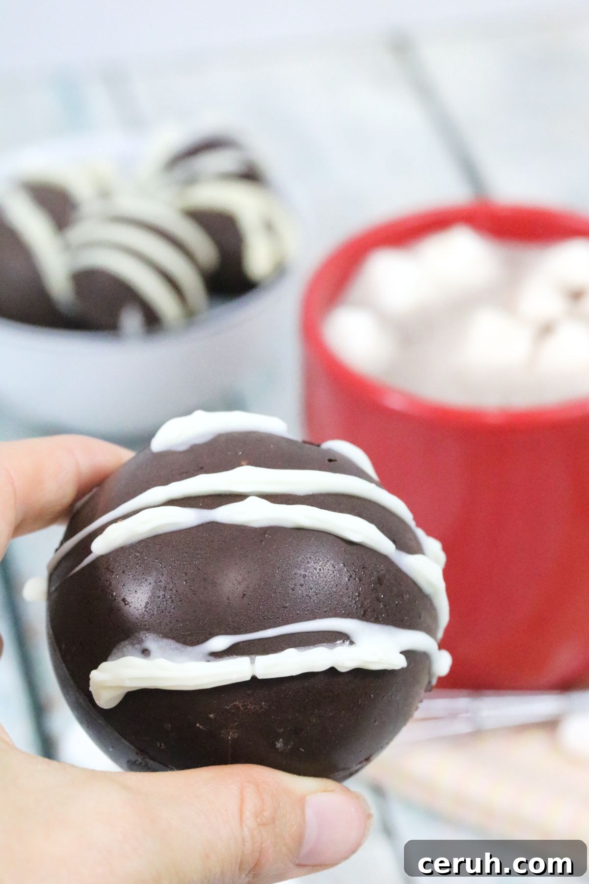 How chocolate bomb with white icing being held between two fingers.