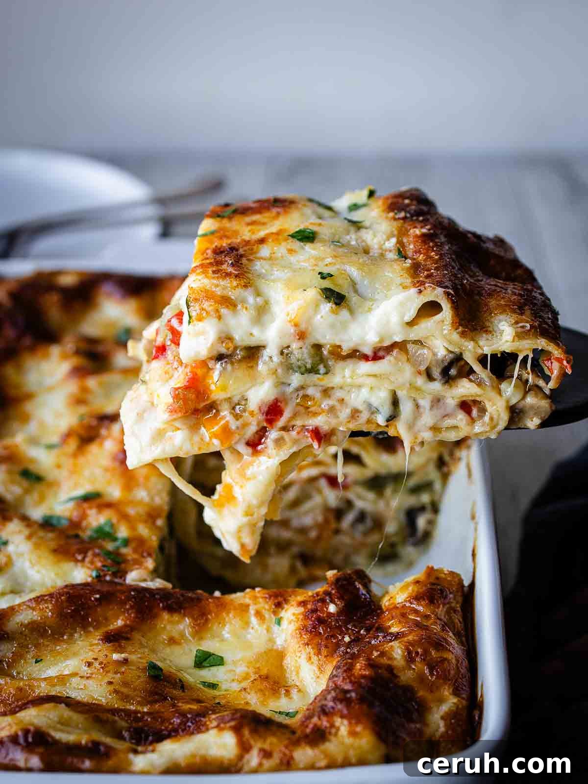 A slice of vegetable lasagna with white sauce being lifted out of a baking dish.