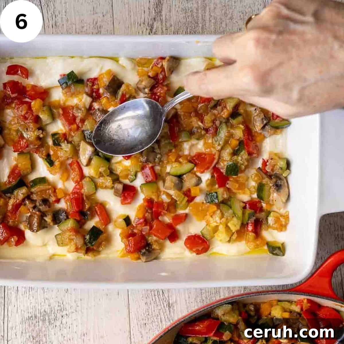 Spreading a mixture of cooked vegetables over white sauce and lasagna noodles in a lasagna pan.