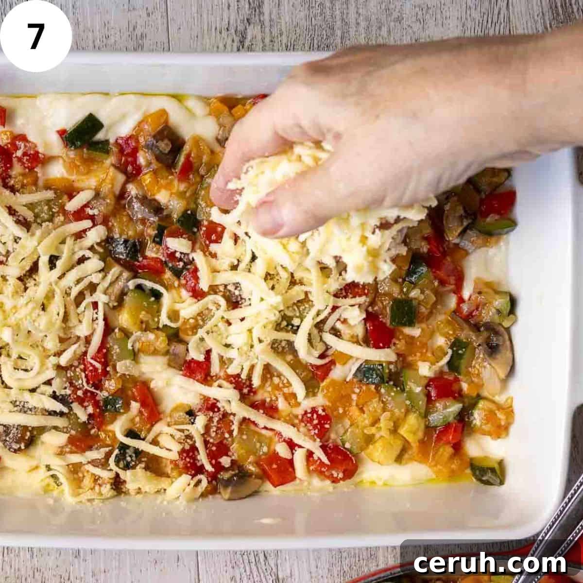 Sprinkling cheese over cooked mixed  vegetables in a lasagna dish.