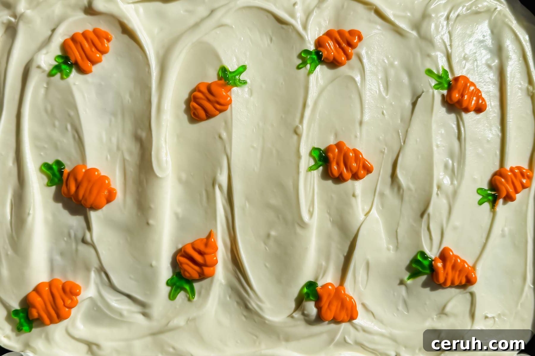 cream cheese frosted carrot cake with small piped colorful carrots on top.