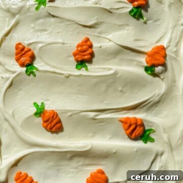 cream cheese frosted carrot cake with small piped colorful carrots on top.