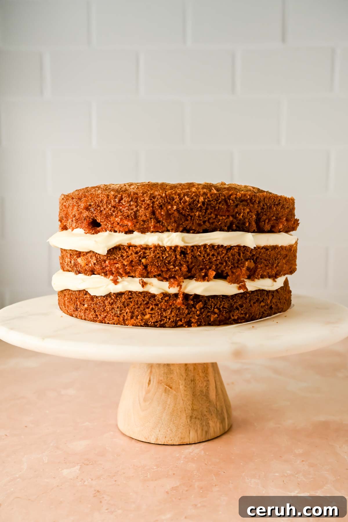 three layered carrot cake frosted between layers on marble cake stand. 