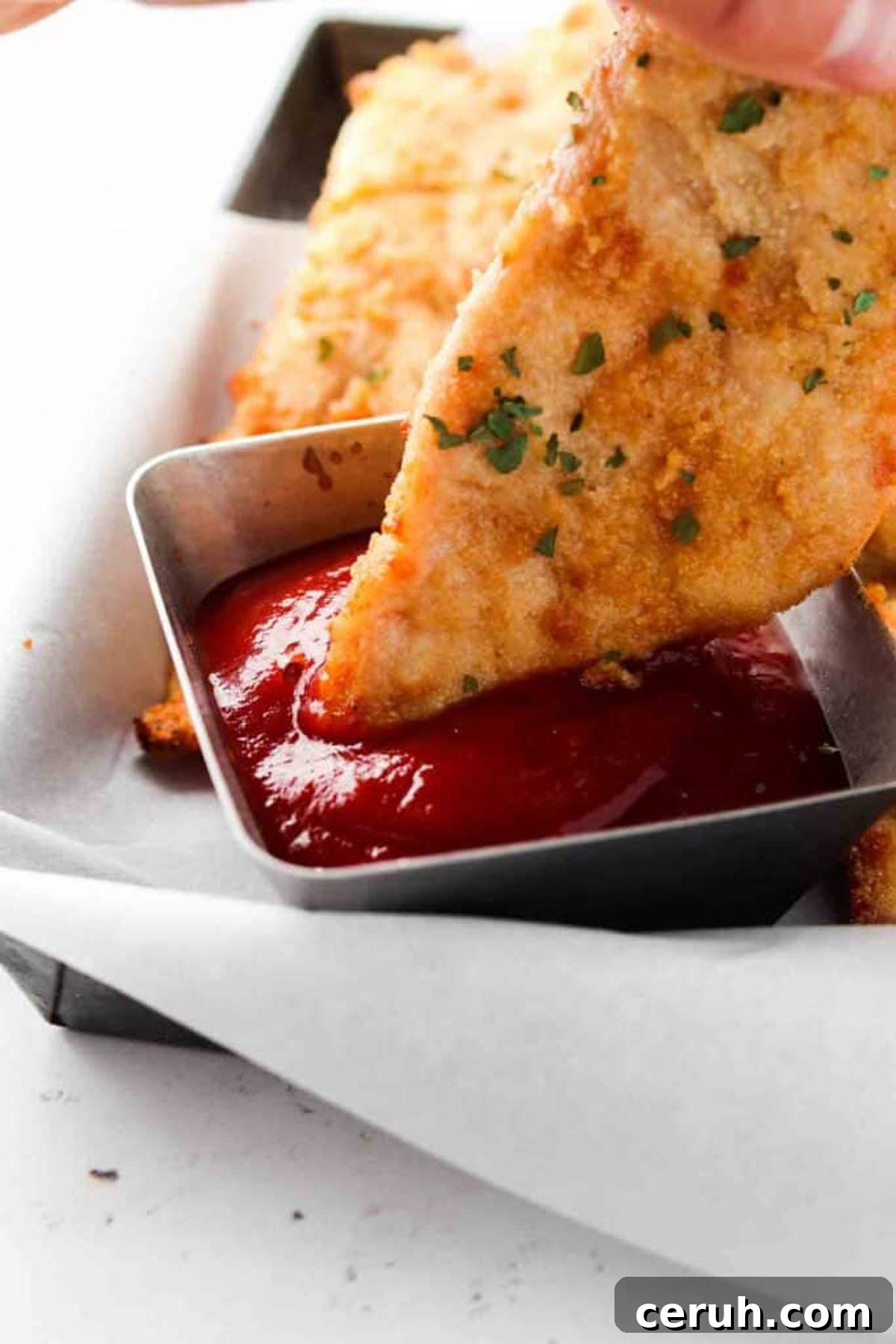 Homemade keto chicken tender being dipped in sauce.