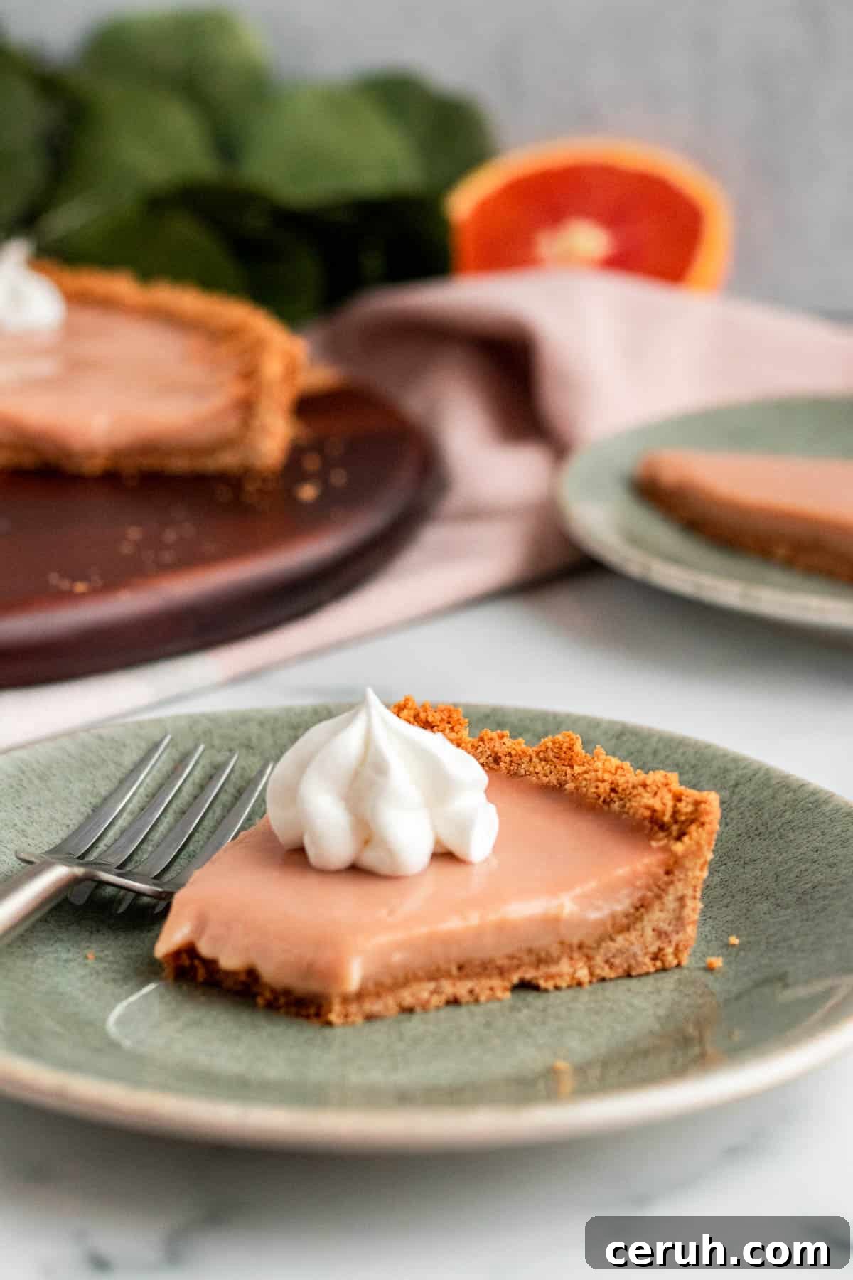 Zesty Blood Orange Tart Recipe with Buttery Shortcrust 4 Slice of blood orange tart topped with a dollop of meringue on a green plate. Full tart and another slice on a plate in the background.