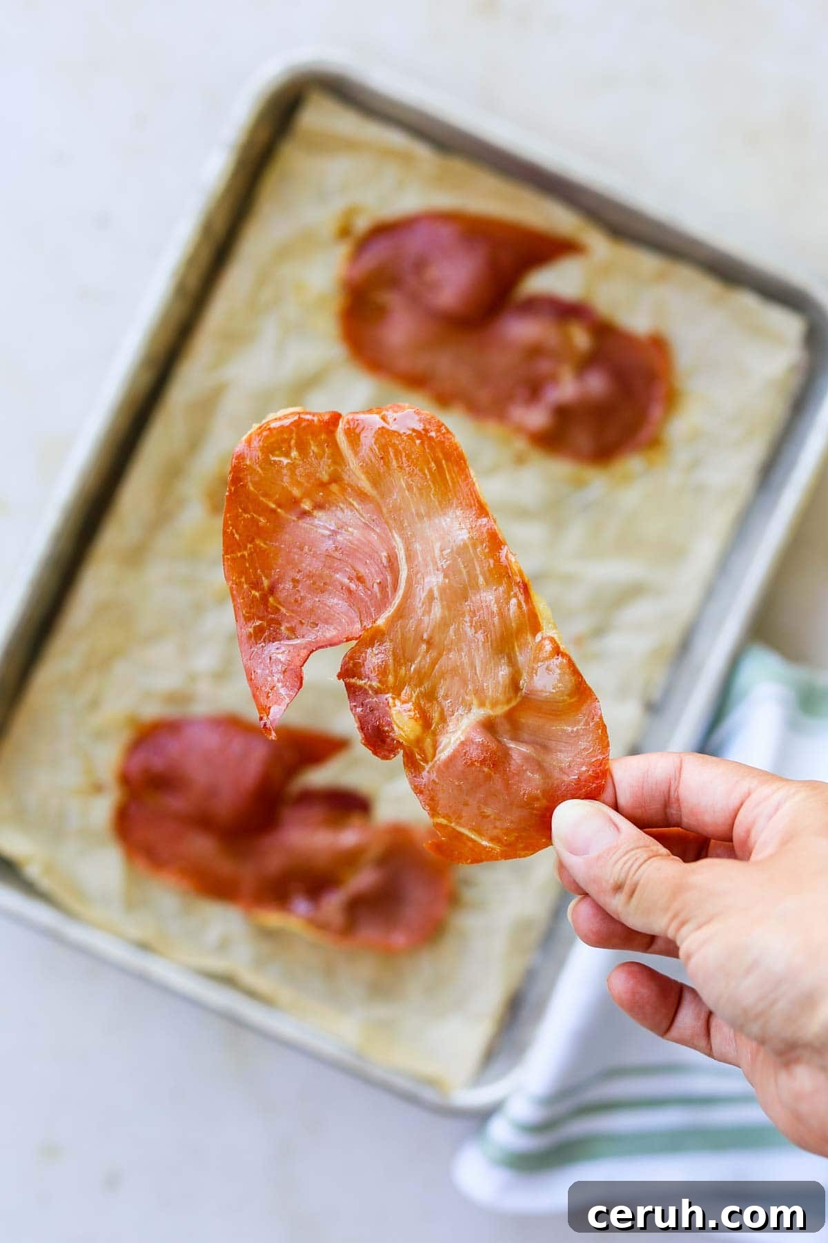 Hand holding a piece of oven-roasted crispy prosciutto.