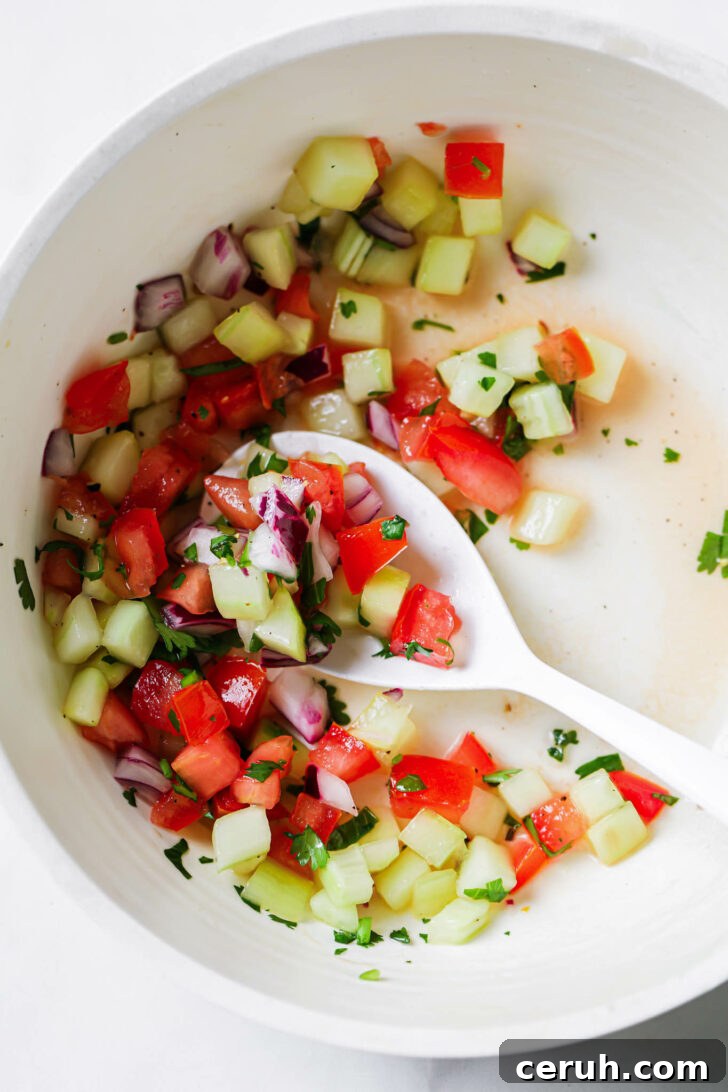 Partially eaten Kachumber Salad in a white bowl with a white spoon.