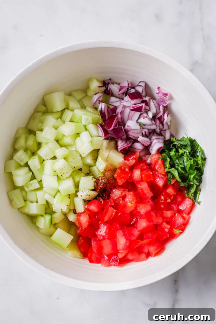 Diced cucumber, tomato, red onion, cilantro with some spice in a white bowl.