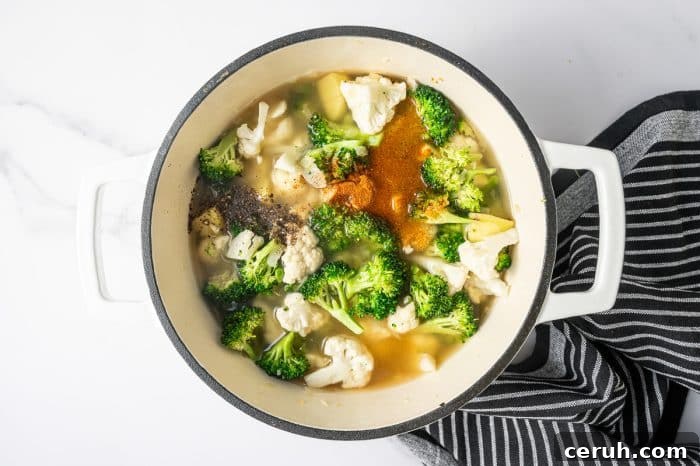 Overhead shot of a cream enameled Dutch oven filled with broth covering broccoli, cauliflower, and potato pieces.
