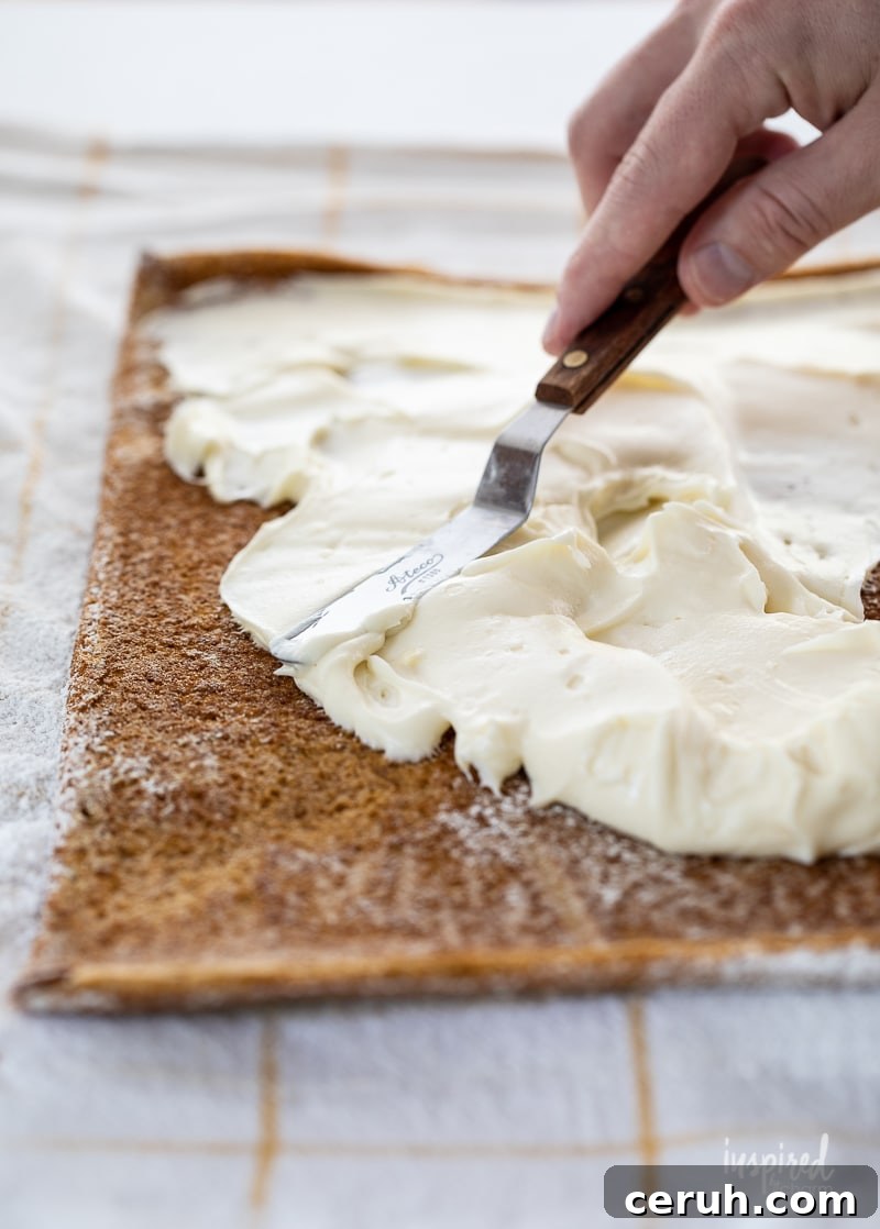 hand spreading cream cheese frosting onto pumpkin roll.