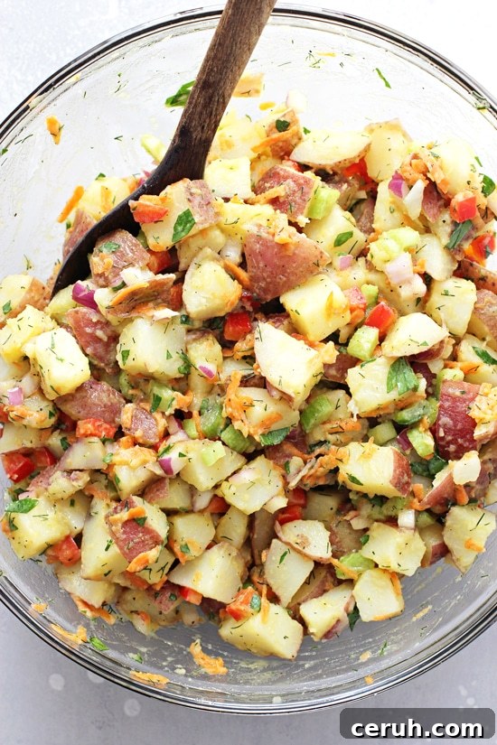 A glass mixing bowl filled with Healthy Potato Salad with a wooden spoon in the dish.