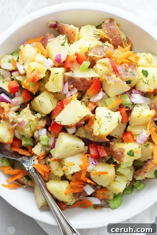 A white bowl filled with No Mayo Potato Salad with a serving spoon in the dish.