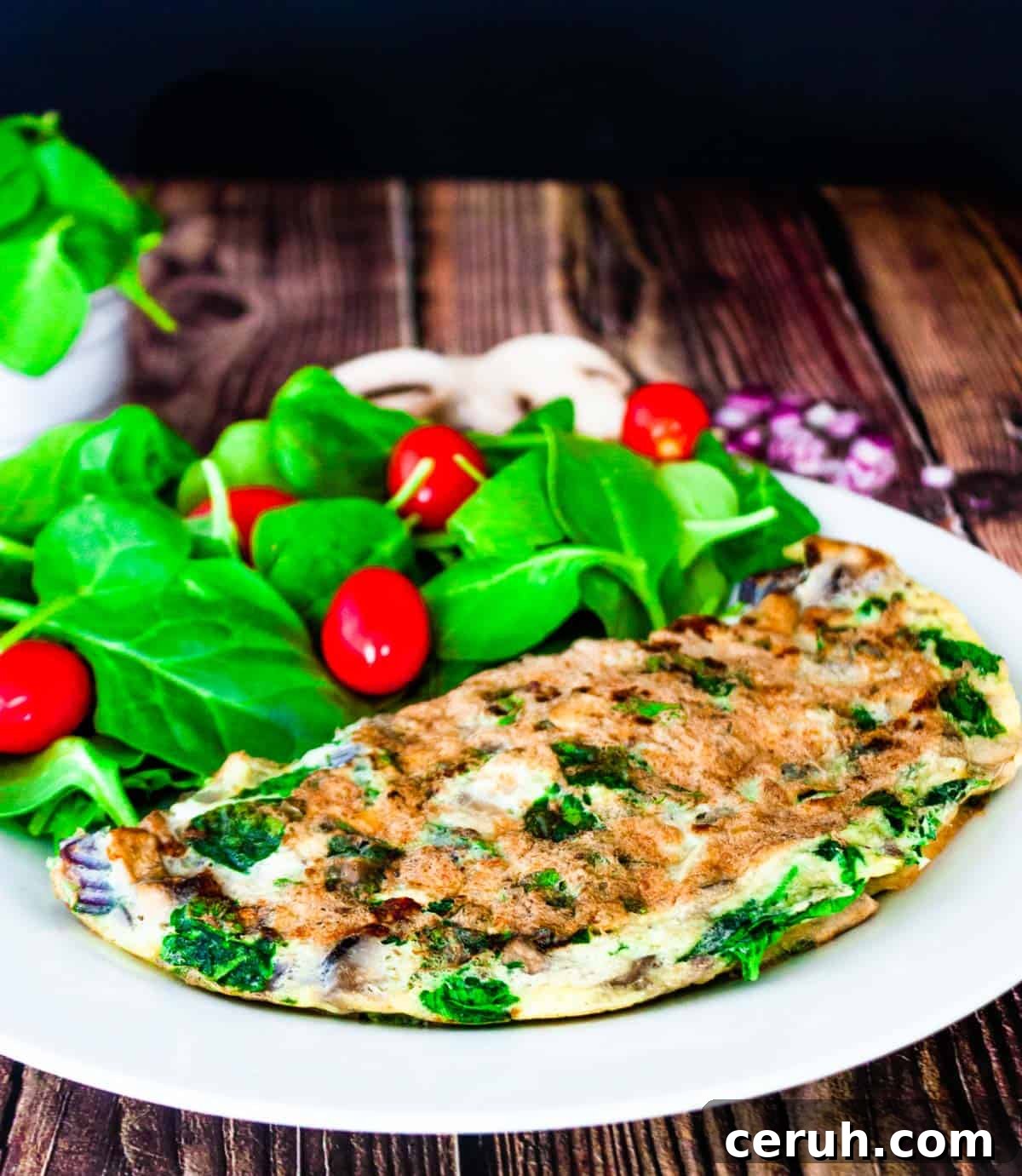 A spinach omelette on a white plate with a side of spinach salad.