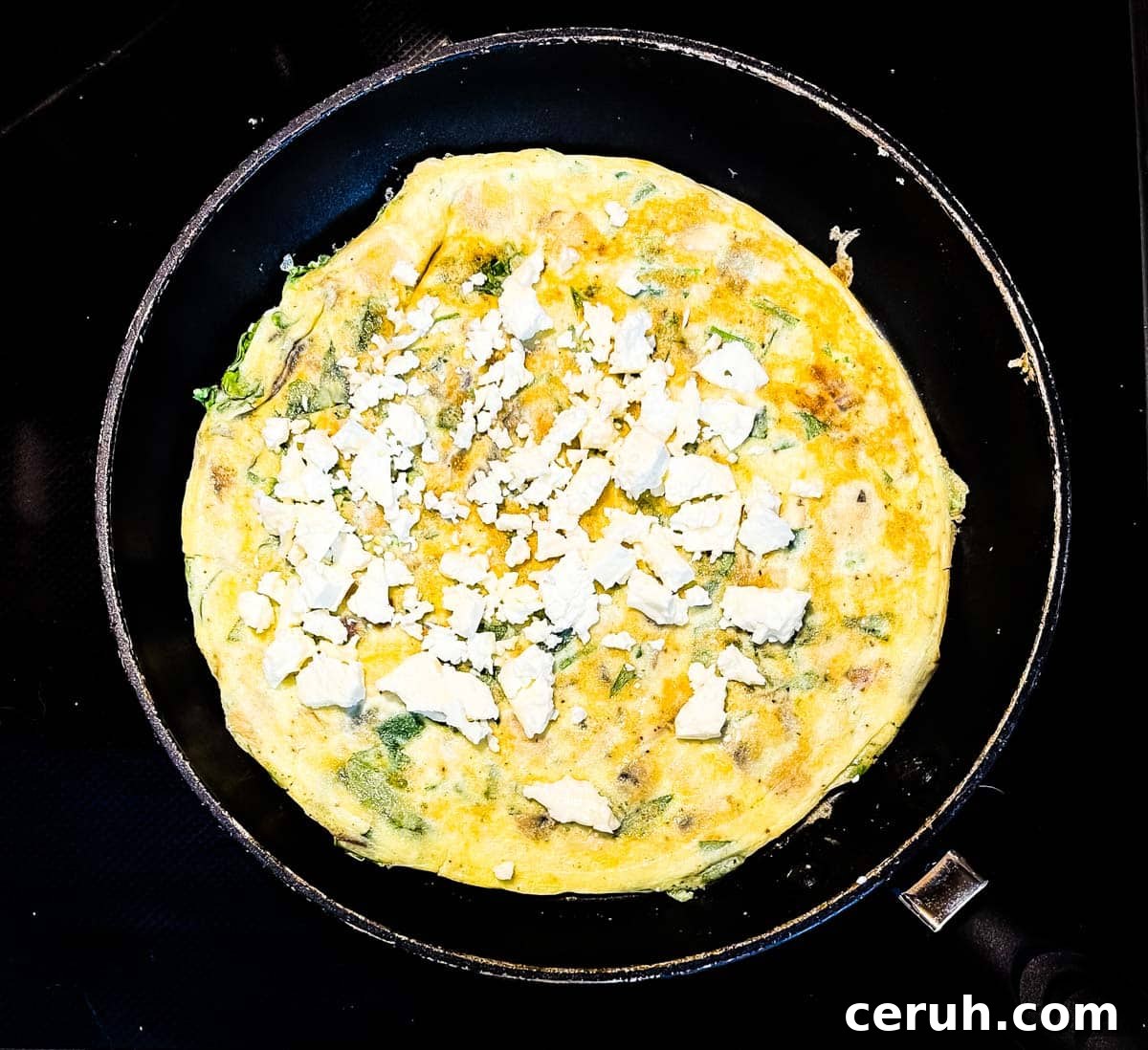 The feta cheese is crumbled and spread evenly on top of the omelette.