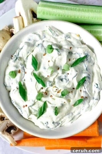 A white bowl filled with creamy keto spinach dip, surrounded by carrots, mushrooms, and celery.