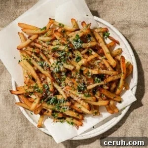 Crispy Parmesan Truffle Fries Recipe — Golden, Flavorful Fries 8 A plate of crispy fries topped with Parmesan cheese and herbs, served on parchment paper.