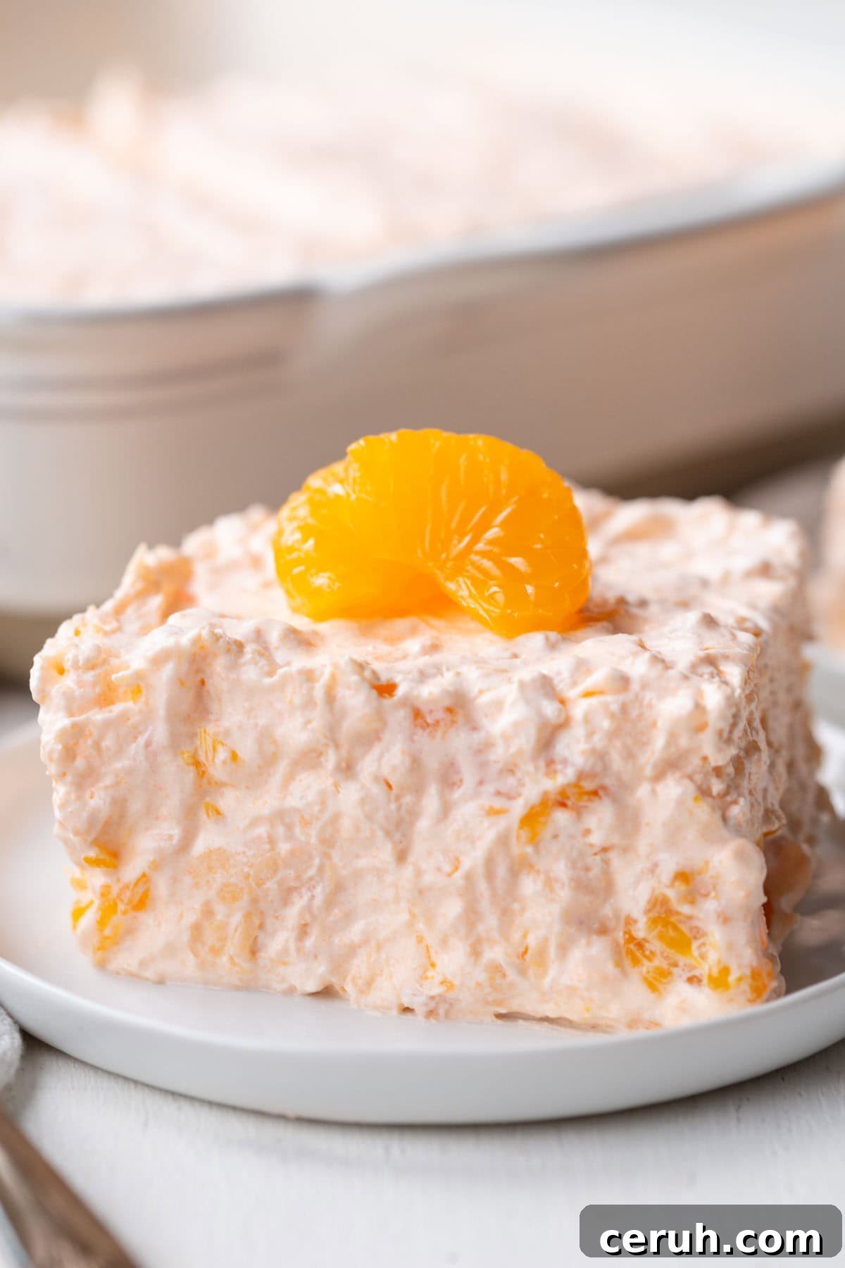 slice of fluffy, creamy gelatin salad with mandarin oranges inside and on top.