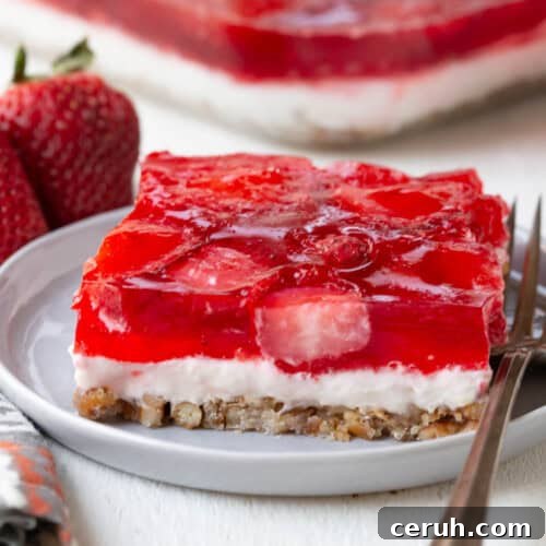 slice of a layered dessert with a pretzel crust, cream cheese filling, and strawberry gelatin on top.