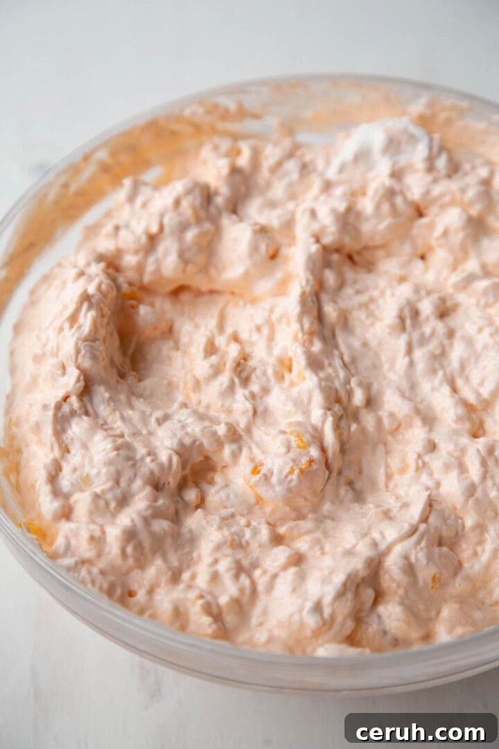 fluffy cottage cheese and orange gelatin mixture with whipped topping in a bowl.