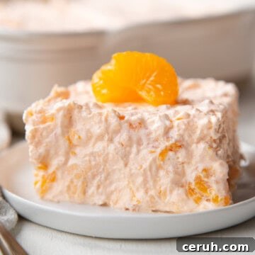 slice of a fluffy gelatin salad with pieces of mandarin oranges inside and on top.
