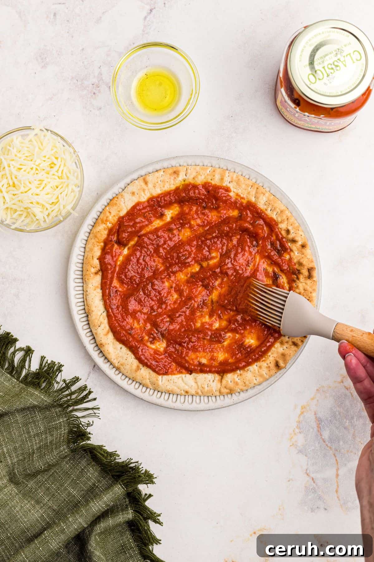 Pizza sauce being brushed over a slice of pita bread on a marble table. 