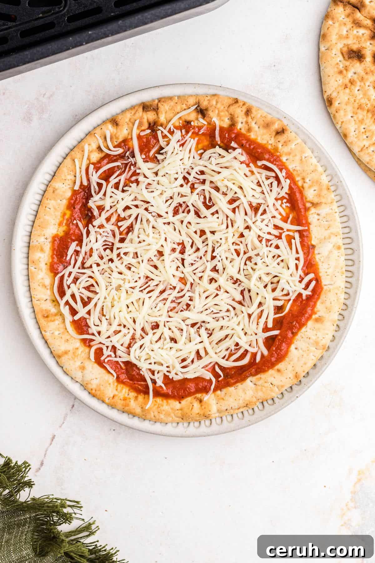 Sauce and shredded cheese on pita bread before cooking in the air fryer basket. 
