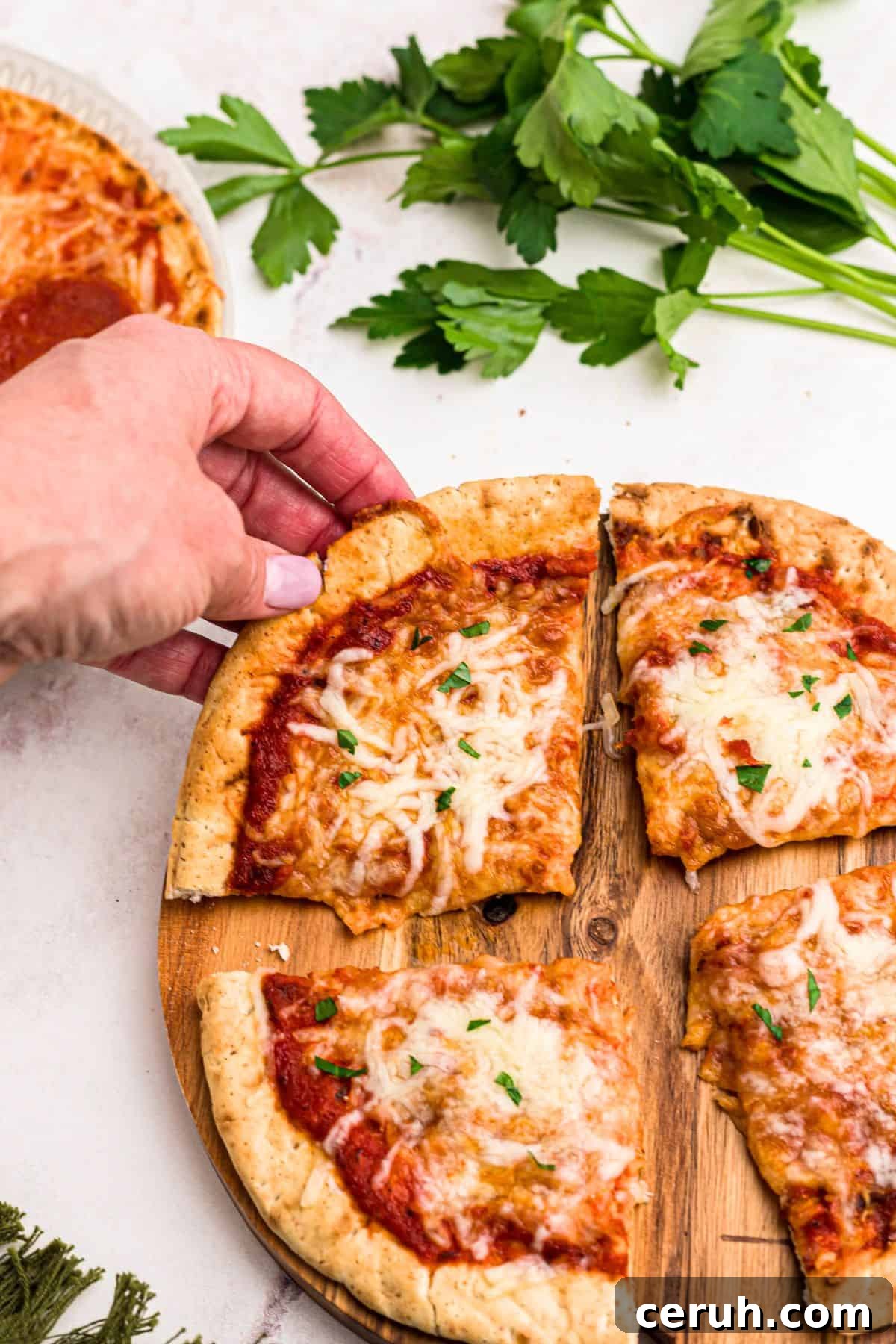 Slice of pita pizza being lifted off of cutting board on a marble table. 