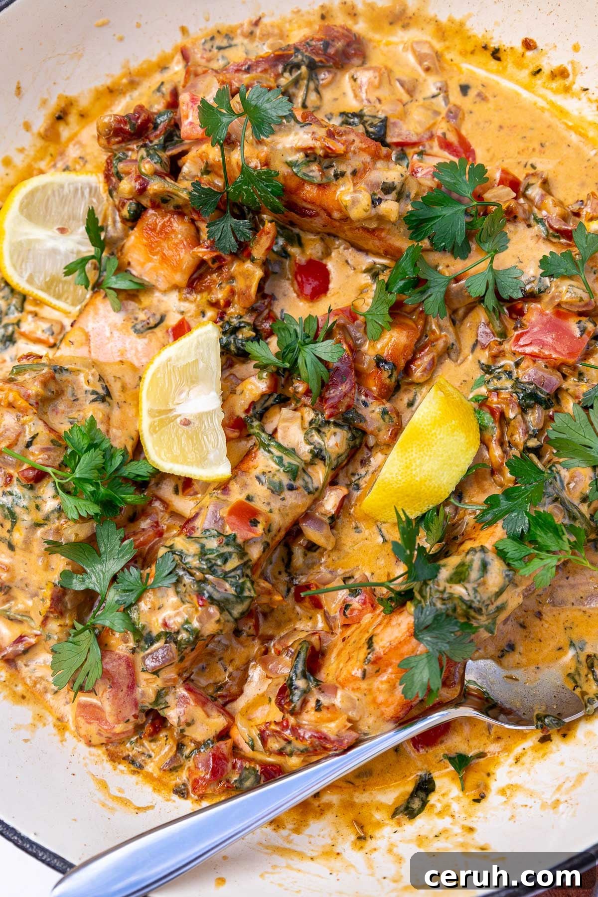 Closeup of the top of the dish sprinkled with parsley and dotted with lemon segments, with a serving spoon.
