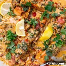 Closeup of the top of the dish sprinkled with parsley and dotted with lemon segments, with a serving spoon.
