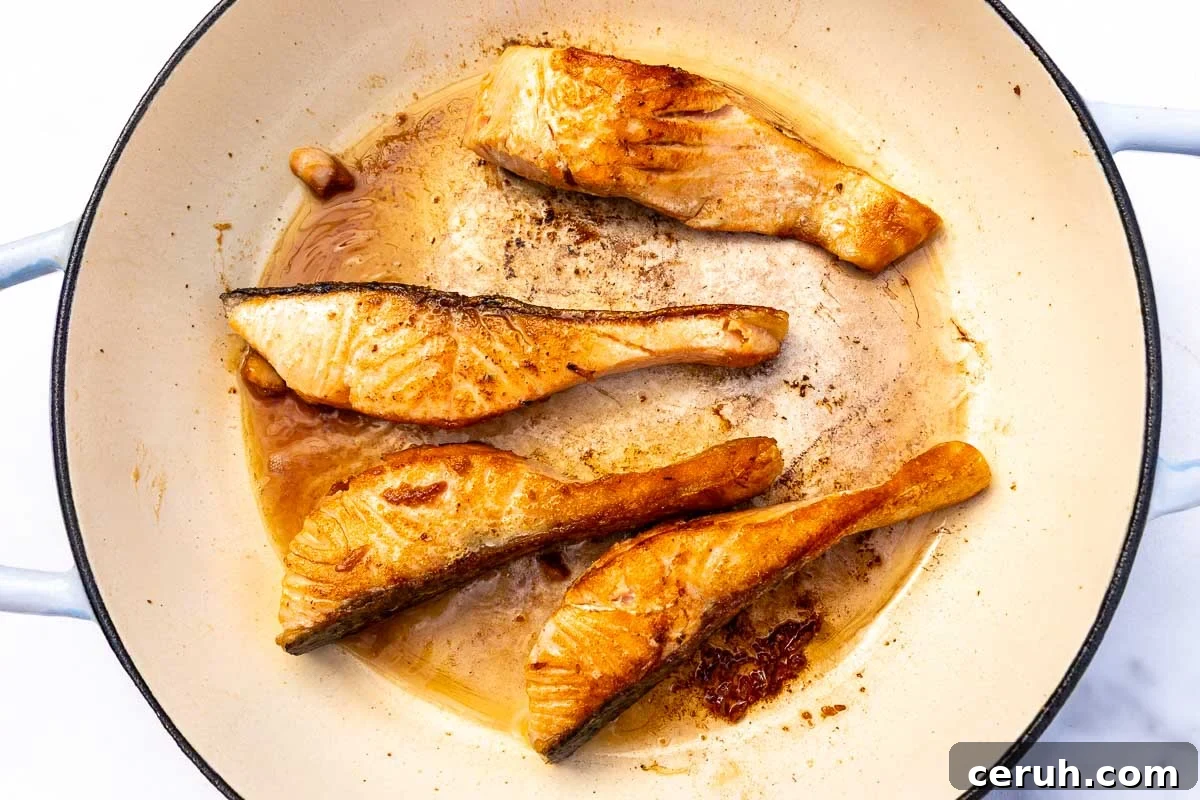 Four pieces of cooked salmon in a pan.