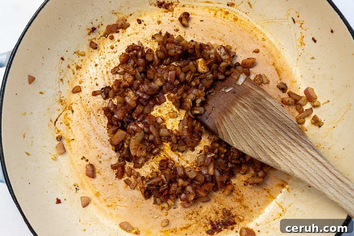Overhead of chopped cooked onions and spices in a cast iron pan with a wooden spoon.
