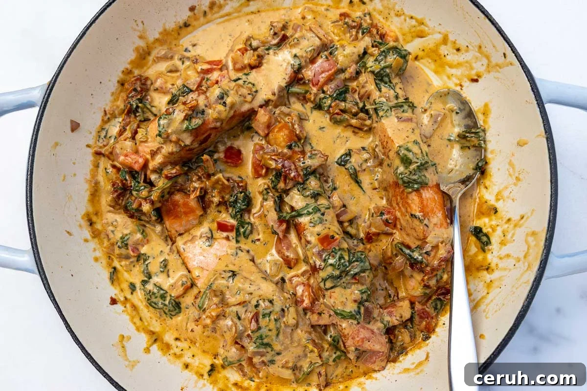 An overhead view of salmon in a tomato cream sauce in a big blue cast iron pan with a spoon.