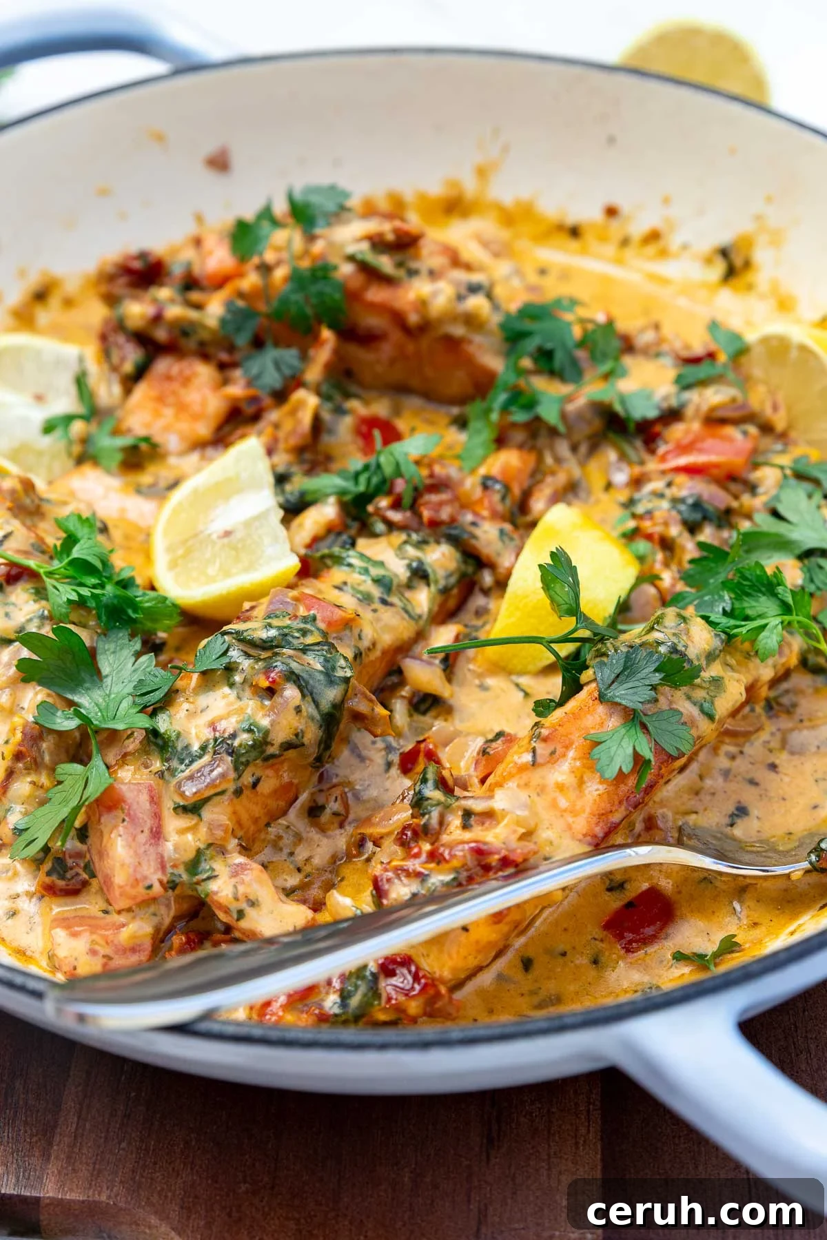 Closeup of salmon in a pan with a cream tomato sauce in a light blue pan and with a serving spoon.