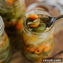 multiple mason jars filled with Mexican escabeche on a wooden cutting board with the closest one with a spoon in it fishing out a serving.