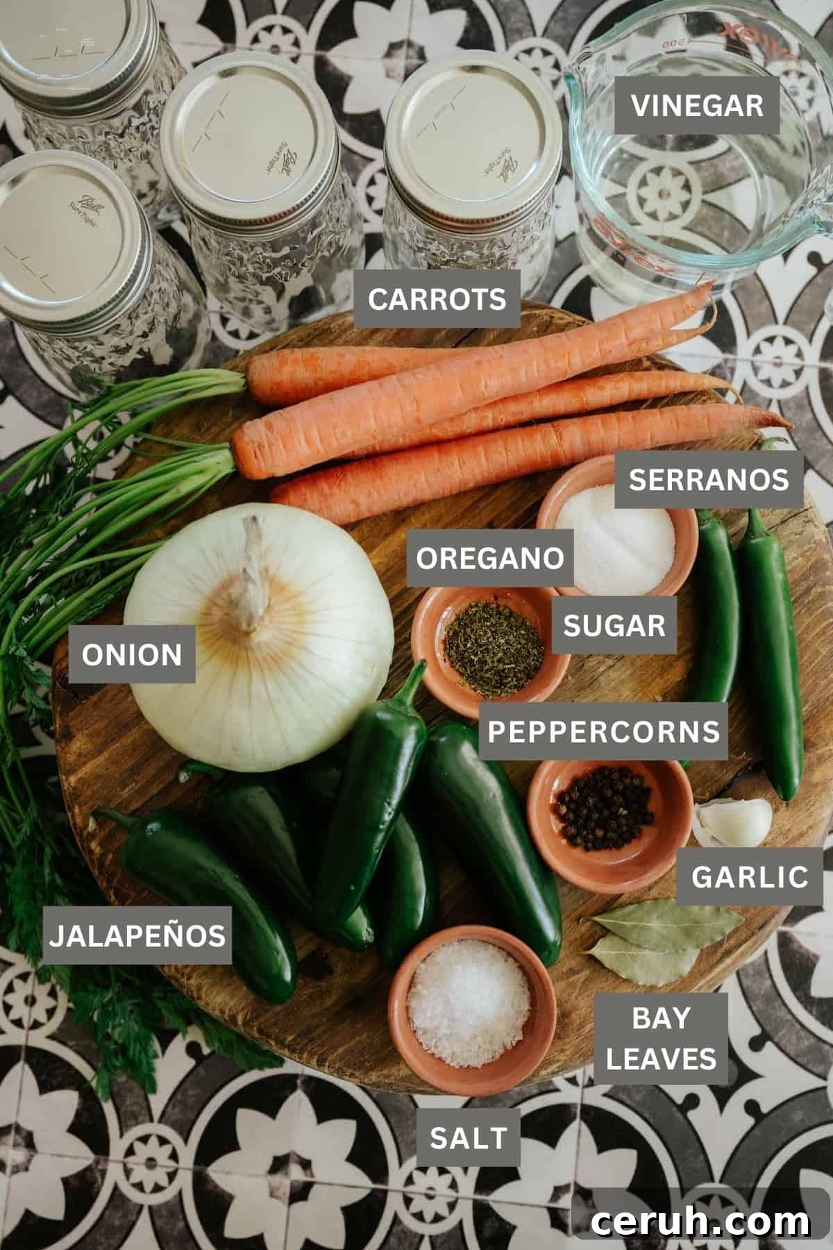 Carrots and chile peppers with spices needed to make Mexican escabeche laid out on a wooden cutting board next to sanitized mason jars for canning. 