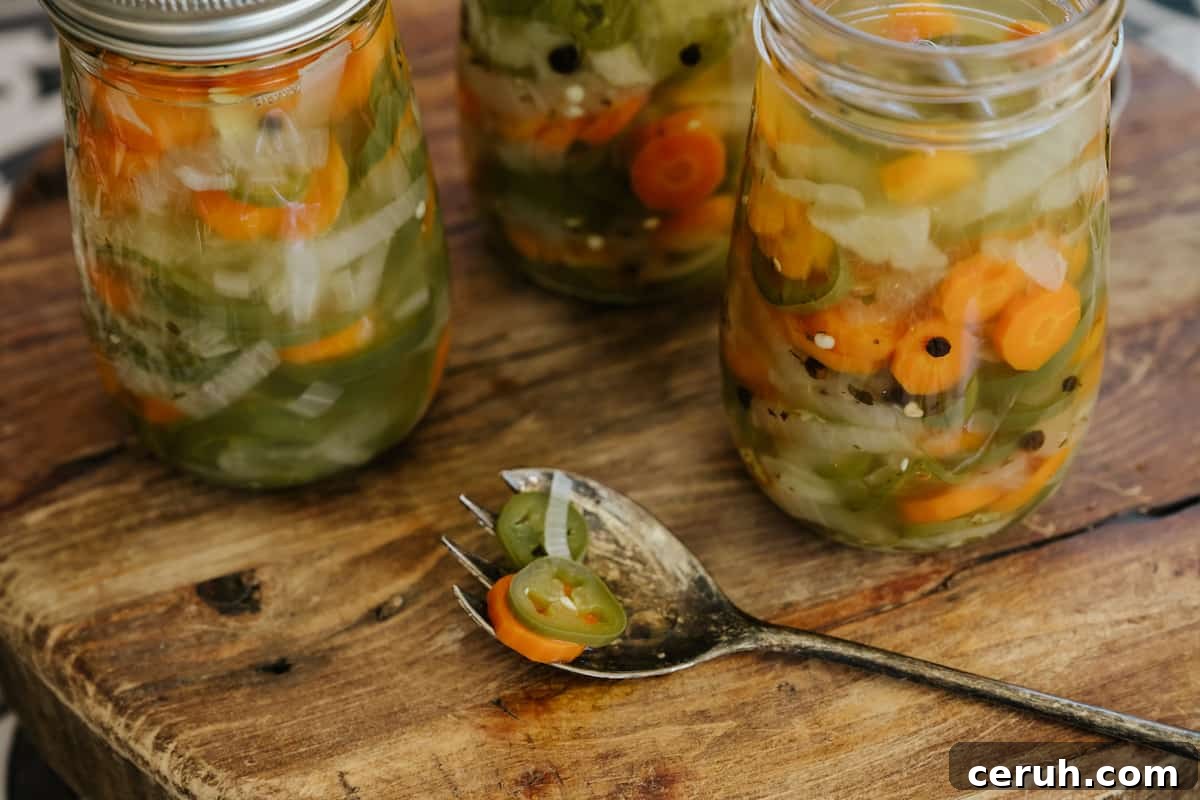 3 jars of homemade jalapeños & carrots in jars on a wooden cutting board with an antique silver serving spoon.