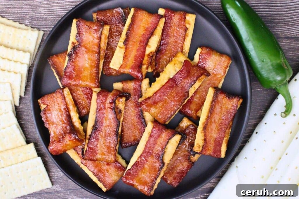 overhead view of bacon crackers on a black plate surrounded by club crackers and a jalapeno