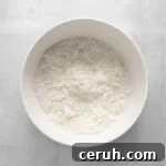 shredded coconut mixed with powdered sugar in a white bowl.