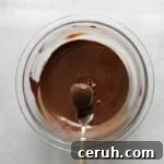 a fork holding a dipped coconut truffle over a bowl of melted chocolate.