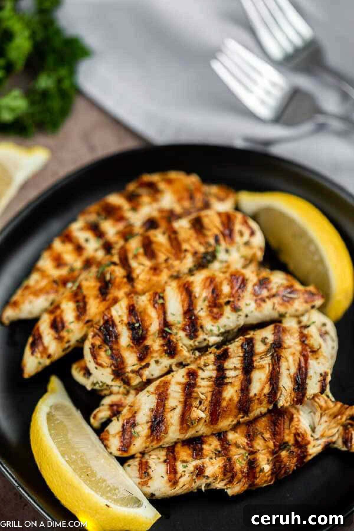 Chicken tenders grilled with grill marks stacked on a plate with lemon wedges on the side. 
