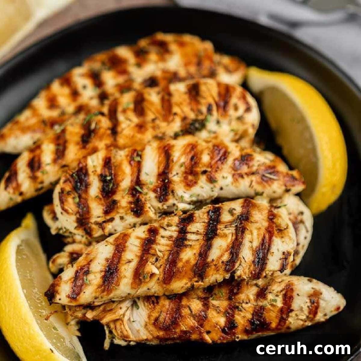 Chicken tenders with lemon wedges on a black plate.