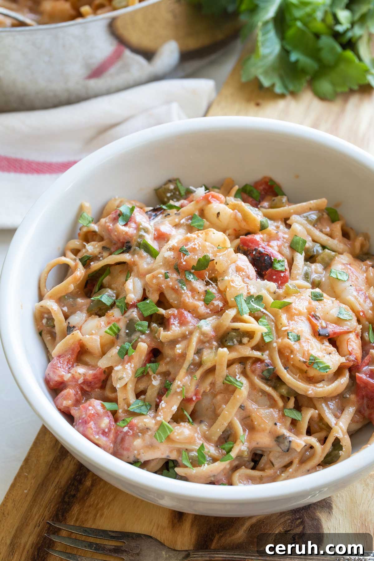 Recipe served in round white bowl, with fork nearby and the rest of the pasta still in pan in background.