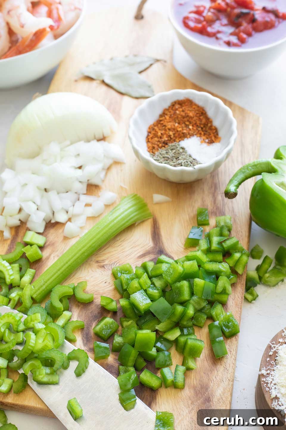 Chopped green peppers, celery and onion on cutting board, surrounded by other ingredients.