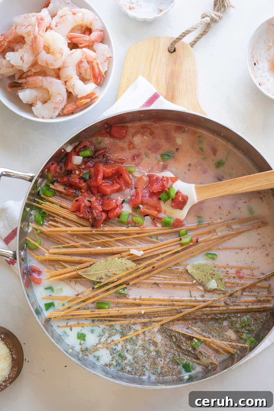 Pot with pasta, liquids, and Cajun spices added, with bowl of raw shrimp waiting nearby.