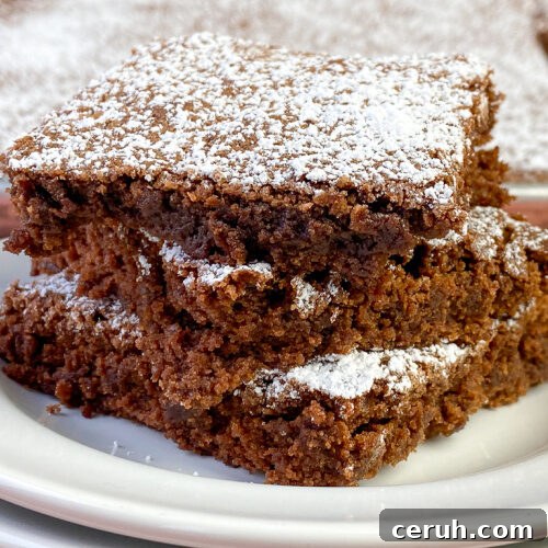 Close up moist brownies stacked up with a thin layer of powdered sugar on top of each piece
