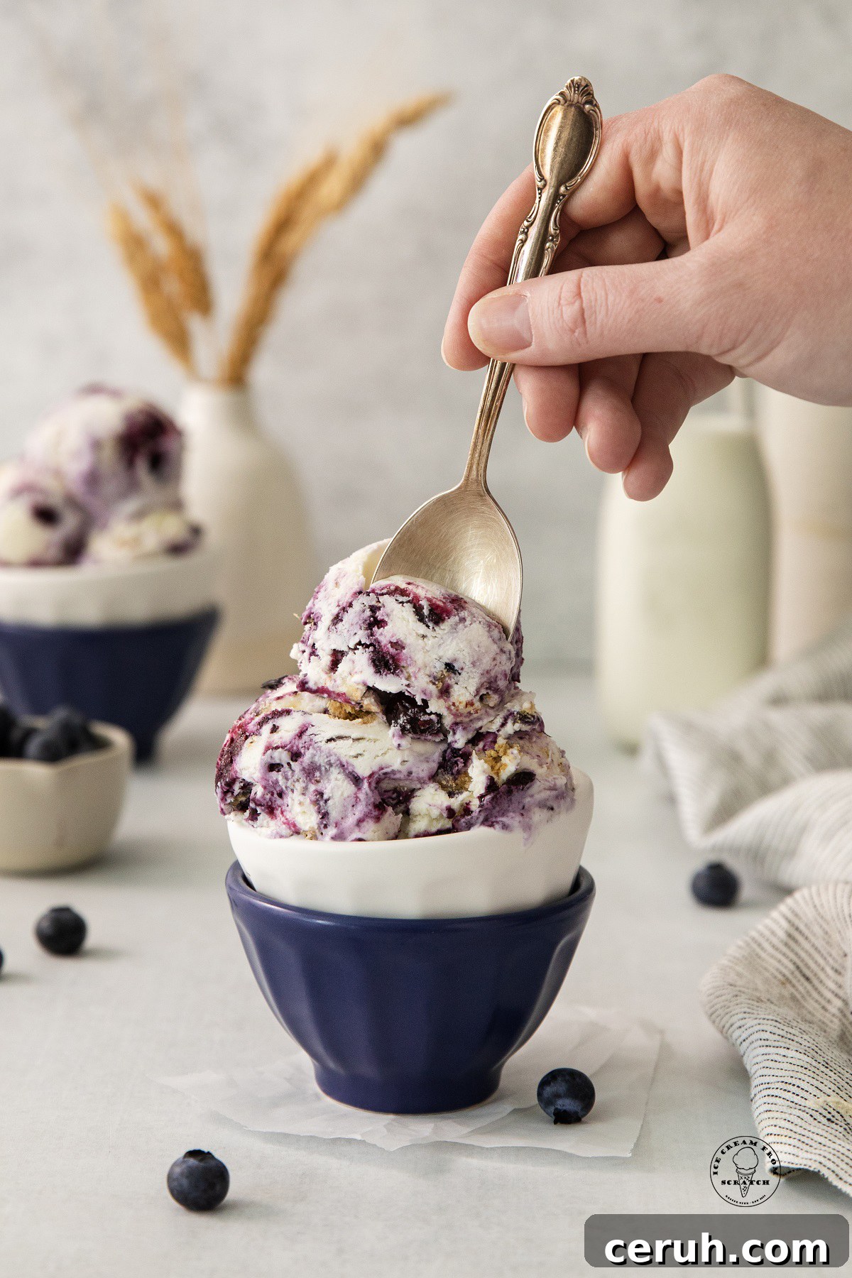 Blueberry Cheesecake Ice Cream Recipe — Creamy Homemade Treat 5 scoops of blueberry cheesecake ice cream in a small bowl, a hand is enjoying it with a spoon